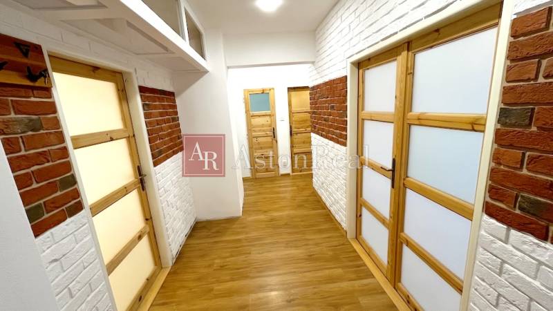A hallway with brick cladding, wooden doors, and a floor with a wooden design in a 3-room apartment.