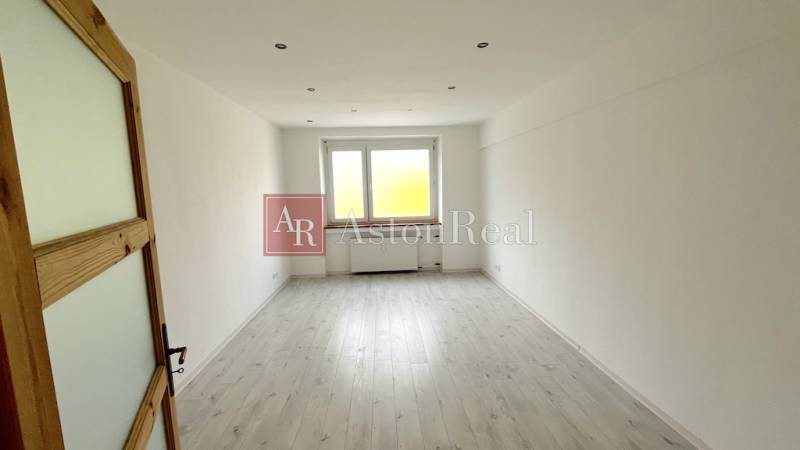 An empty room in a 3-room apartment with a window and a floor with a wooden decor.