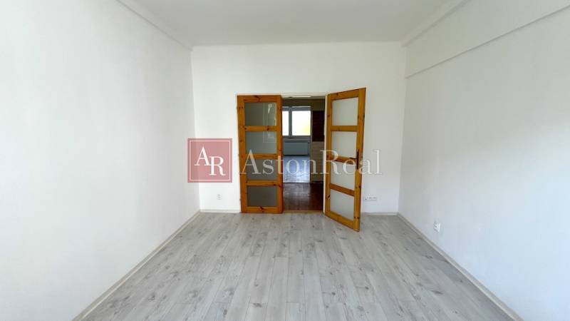 A room in a 3-room apartment with a wooden decor floor, white walls, glass doors.