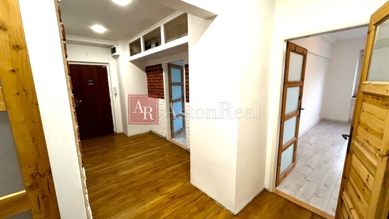 A hallway in a 3-room apartment with a wooden decor floor and brick details.