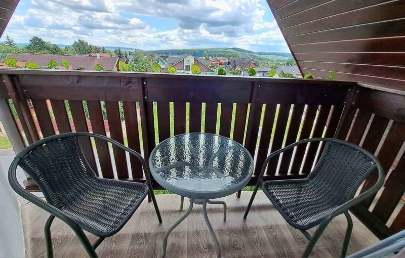 A balcony with rattan chairs and a round table offers a view of Veľká Lomnica.