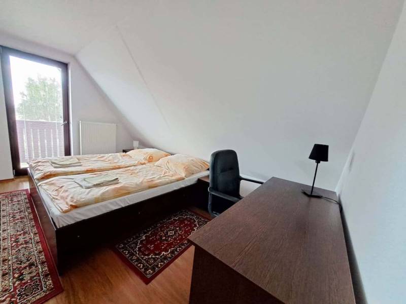 A bedroom with a bed, table, and carpet in a 3-room apartment with a wooden decor floor.