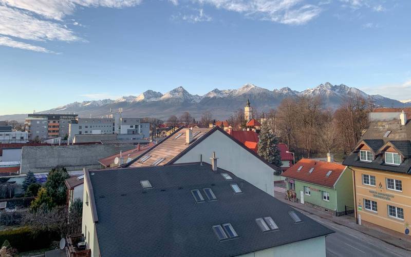View of the High Tatras from Poprad over the rooftops of houses, snow-covered mountains in the distance.