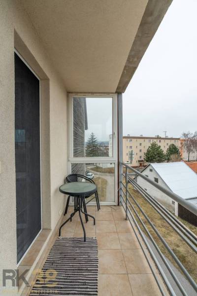 The balcony of a 4-room apartment with a view of Poprad includes a table and a chair.