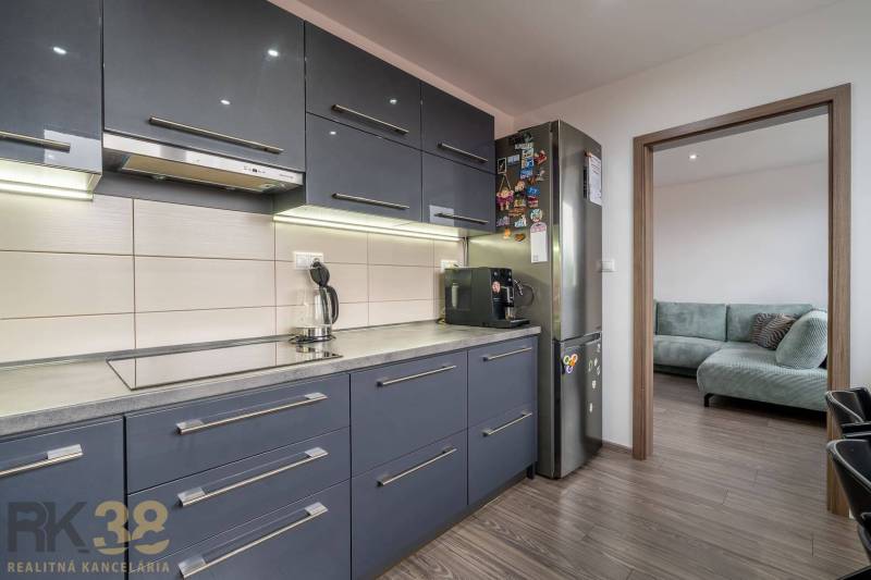 A kitchen in a 4-room apartment with a dark kitchen unit and a floor with a wooden decor.