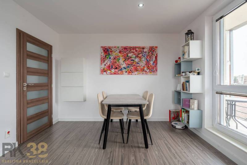 Dining area with a table and paintings in a 4-room apartment with wood-patterned flooring.