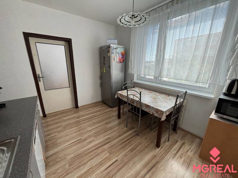 A kitchen in a 3-room apartment with a wooden decor floor, a dining table, and appliances.