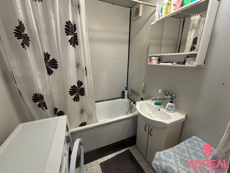 Bathroom with a shower curtain, white furniture, and flooring in a 3-room apartment.
