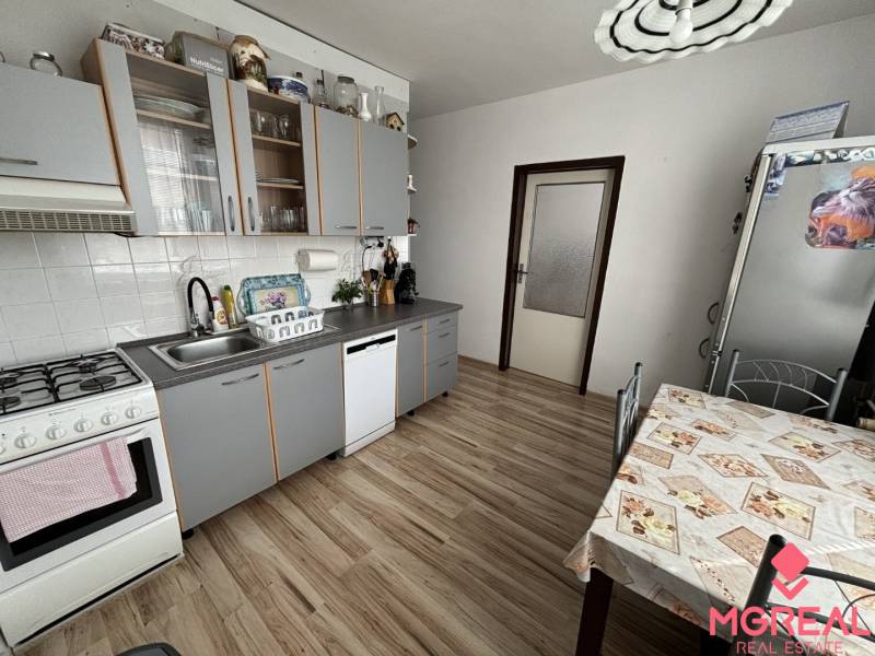 A kitchen in a 3-room apartment with a wood-patterned floor, modern appliances, and a dining table.