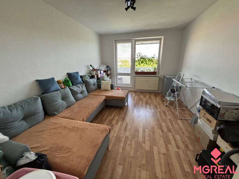 Living room with a sofa and wood-patterned flooring in a three-room apartment.