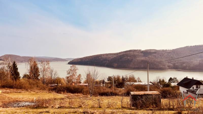 View of recreational plots in Nová Kelča near the water and wooded hills.