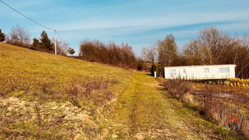 A cottage on a slope surrounded by greenery and trees in the Recreational Lands of Nova Kelc.