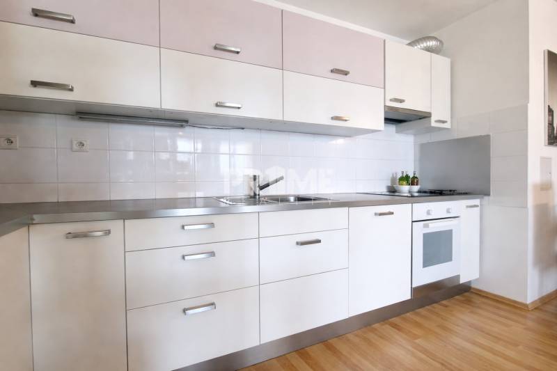 A kitchen in a 2-room apartment with a white kitchen unit and a floor with a wood decor.