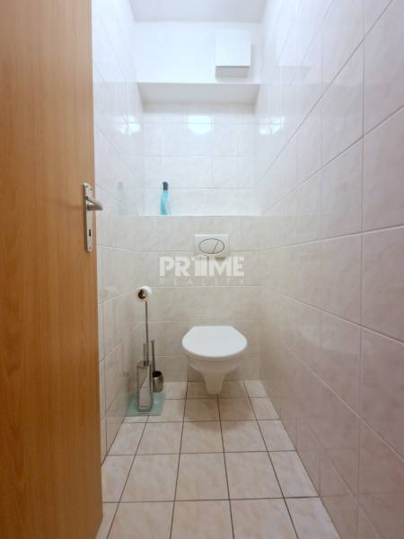 A toilet with white tiles in a 2-room apartment.