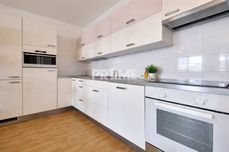 A kitchen unit in a 2-room apartment with a wooden decor floor and white cabinets.
