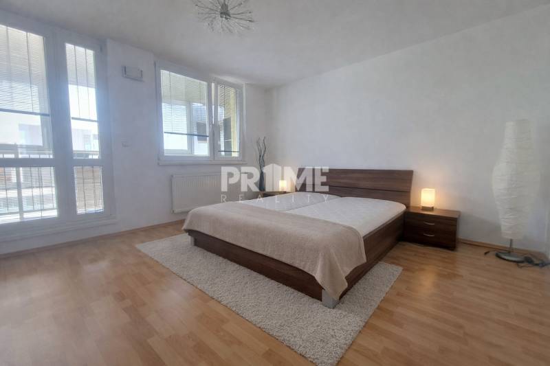 A bedroom with large windows, a double bed, and a wooden decor floor in a 2-room apartment.