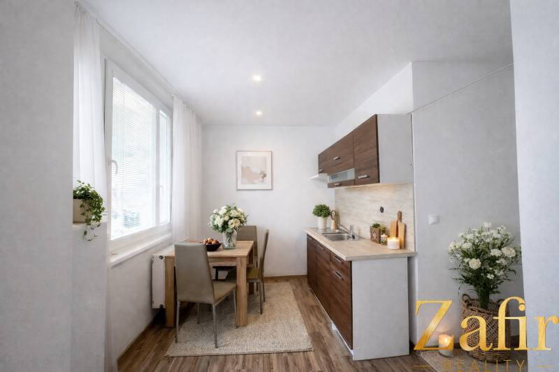 A kitchen in a one-room apartment with a wooden decor floor and flowers on the table.