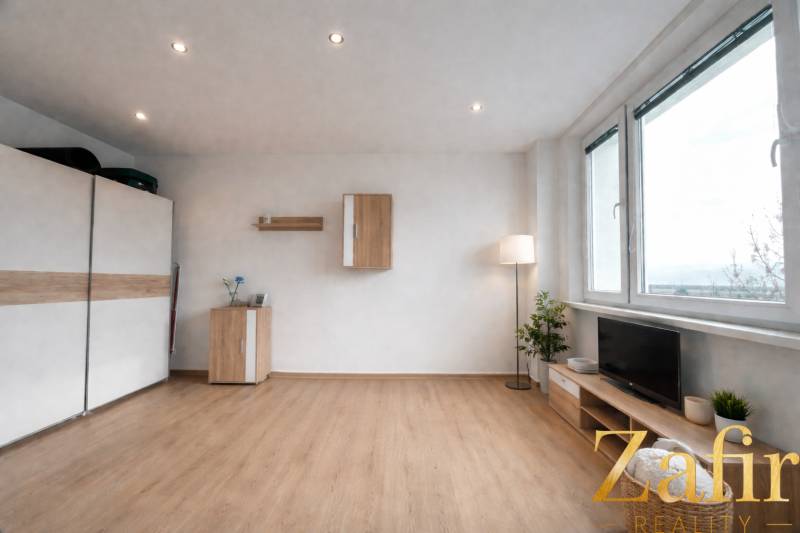 Living area in a studio apartment with wood-patterned flooring and furniture.