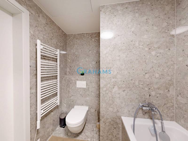 A bathroom in a studio apartment with a bathtub and a wall radiator on grey tiles.