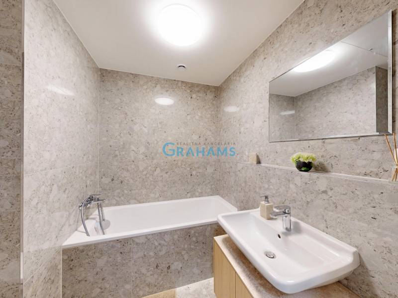 A bathroom with a bathtub and a sink lined with stone tiles in a studio apartment.