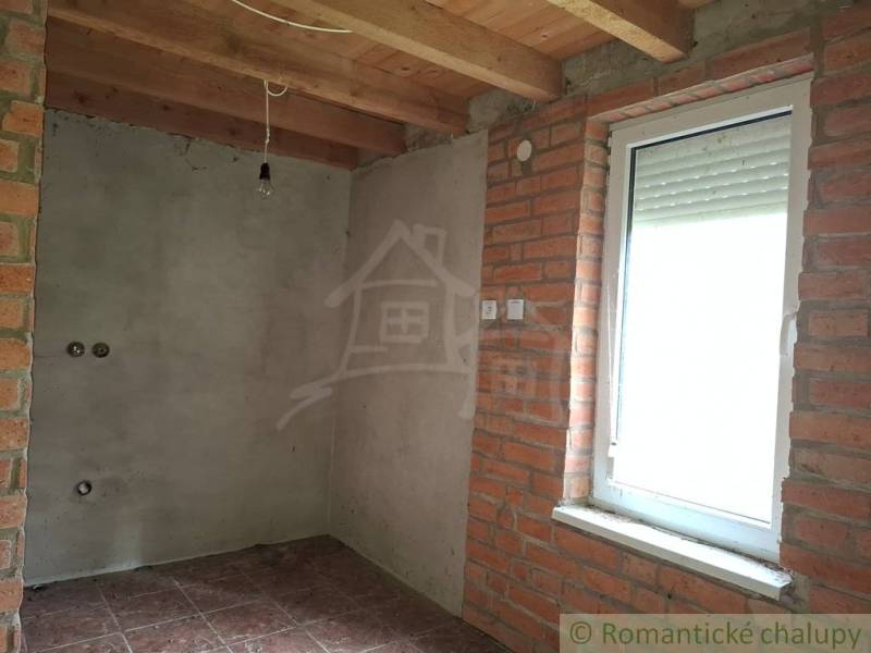 A room in a cottage with a brick wall, wooden ceiling, and a window with a blind.