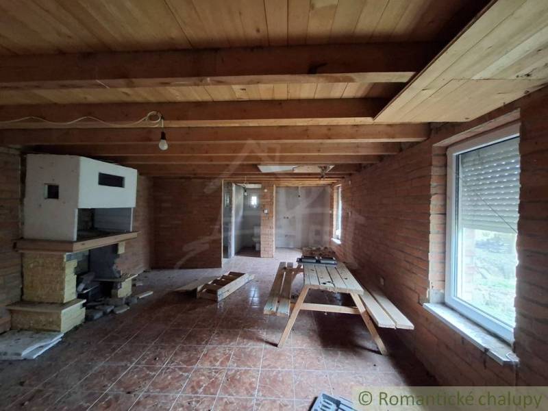 Interior of a cabin with wooden decor, seating area with a table and a fireplace on a brick wall.