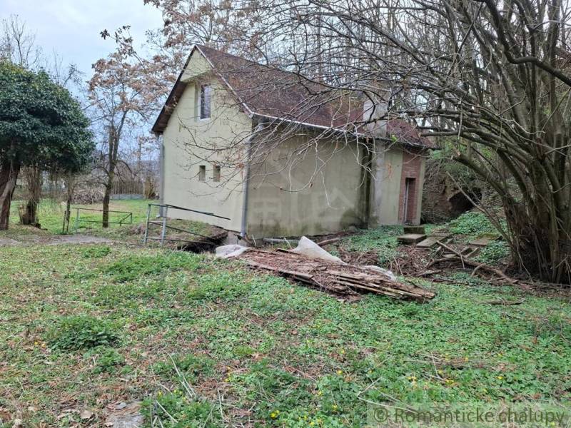 A cottage in Chľaba surrounded by trees and greenery awaits renovation.