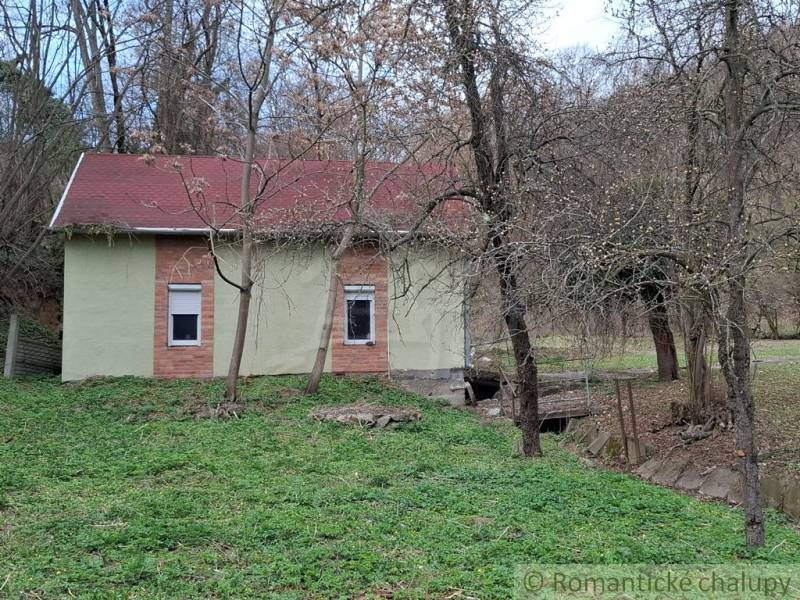 A cottage in Chľaba with trees, greenery, and hilly terrain in the surroundings.