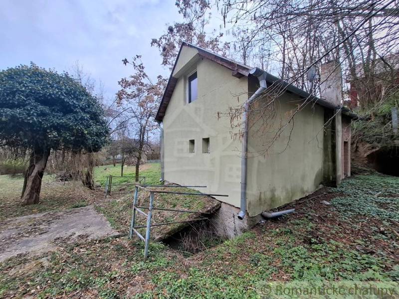 A cottage in Chľaba surrounded by greenery and nature, with a small bridge over a stream.