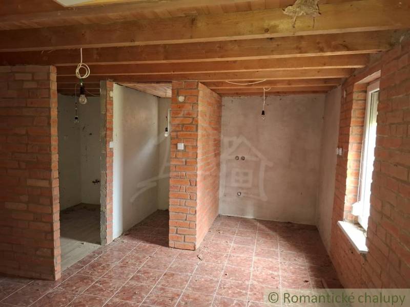 Interior of a cabin with brick walls, wood-patterned flooring, and ceiling beams.