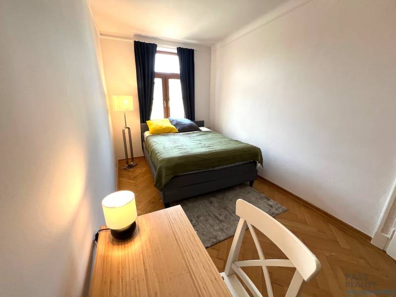 Bedroom in a 2-room apartment with a bed, a desk, and a wooden decor floor.