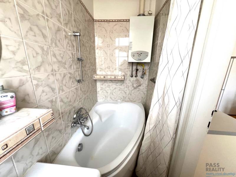 A bathroom in a 2-room apartment with a bathtub and a gas boiler, tiles in light tones.