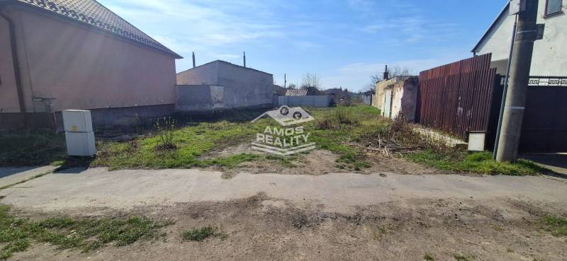 A residential plot on Družstevná in Malacky with an unmaintained grassy surface and buildings around.