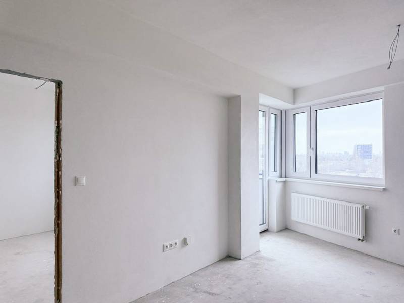 A bright room with large windows in a 3-room apartment without floor coverings.