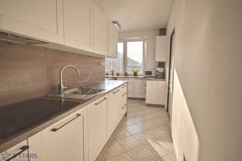 A kitchen with light cabinets and a wood-patterned floor in a three-room apartment.