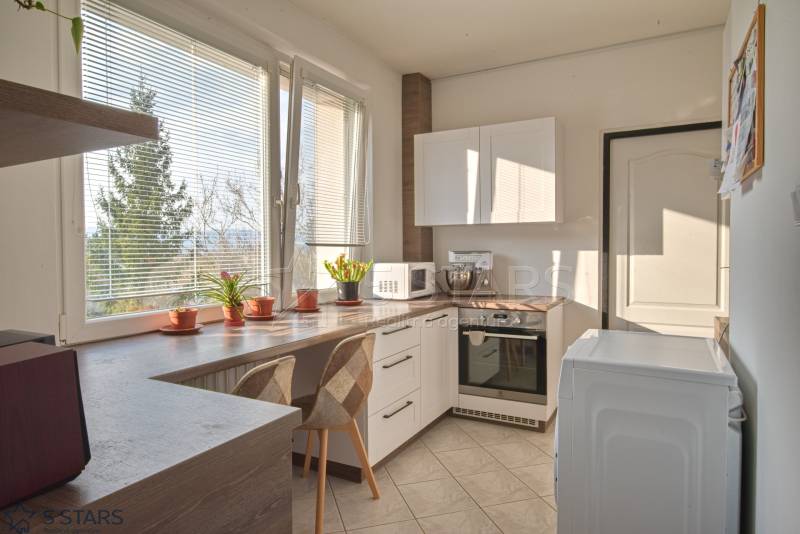 A bright kitchen with a window in a 3-room apartment, plants on the windowsill, seating, and appliances.