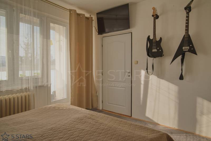 Guitars on the wall in the bedroom of a three-room apartment with a TV on the wall.