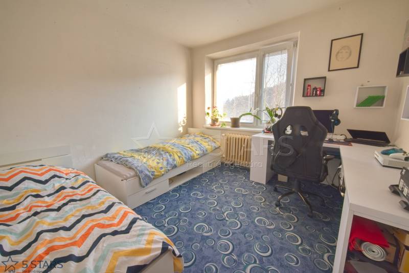 A room in a 3-room apartment with carpeted flooring, a desk, and beds.