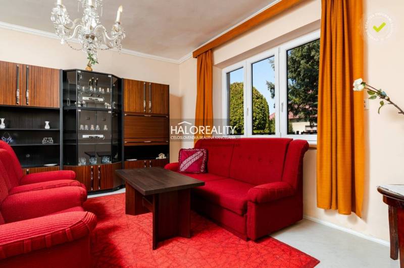 A living room in a family house with red furniture, a crystal chandelier, and a window.