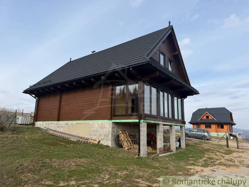 The family house in Lom nad Rimavicou is wooden with a black roof and large windows.