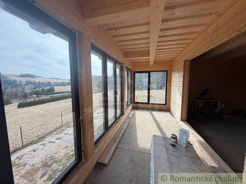 Interior of a family house with wood-patterned flooring and large windows, surrounding fields.