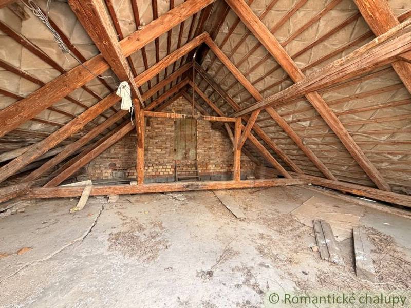 The attic of a family house in Čalovec with exposed wooden beams and a brick wall.
