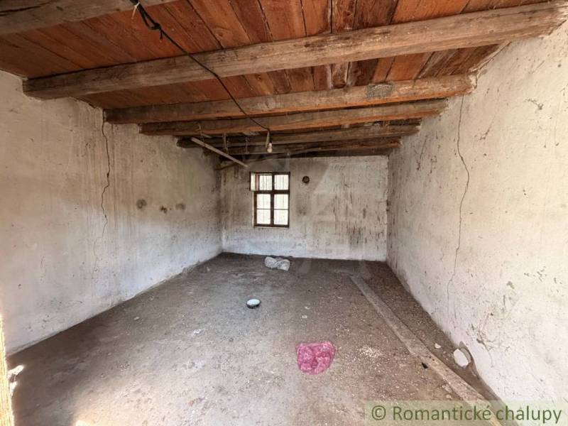 A shabby room in a family house with a wooden beam ceiling and a small window.