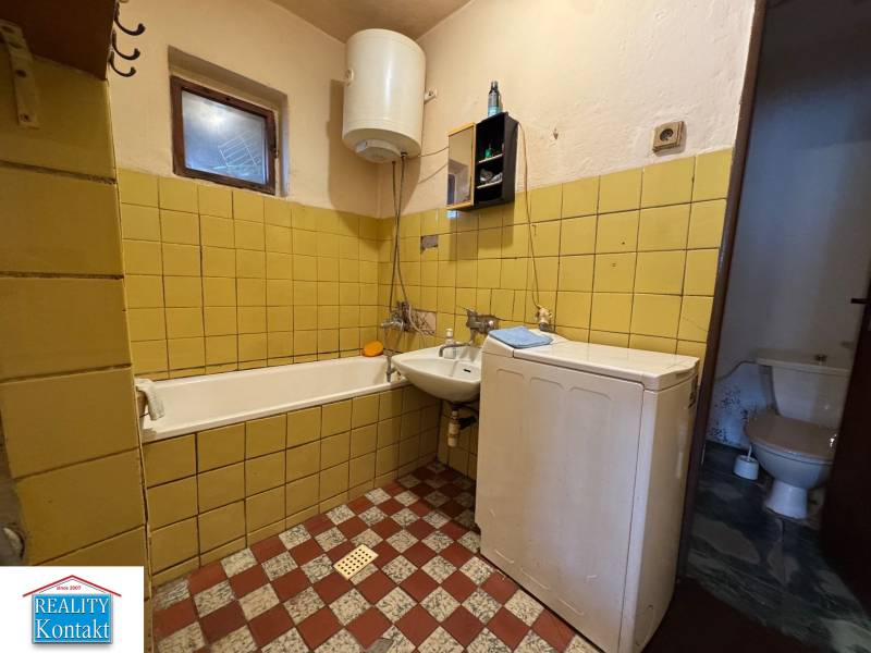 A bathroom in a family house with a bathtub, sink, and washing machine, yellow tiles on the walls.