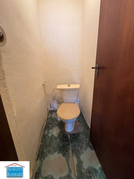 A bathroom in a family house with a toilet and dark tiles on the floor.