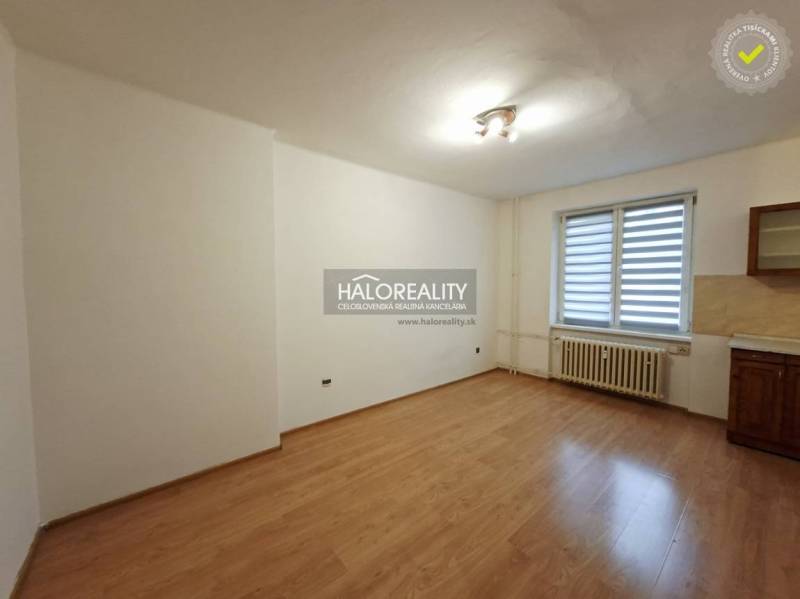 A room in a studio apartment with a wood-patterned floor and simple lighting.