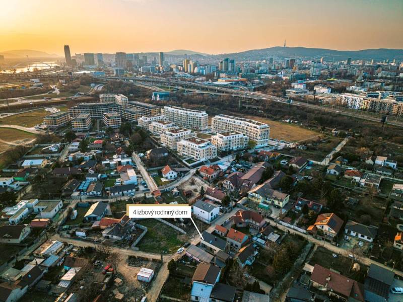 An aerial view of a neighborhood with family houses and the panorama of Bratislava at sunset.