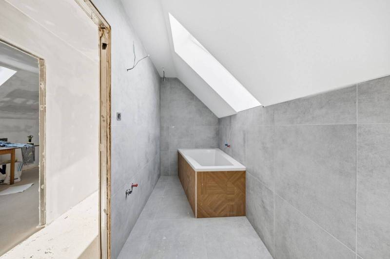 A bathroom in a family house with a bathtub and a skylight, white wall, gray tiles.