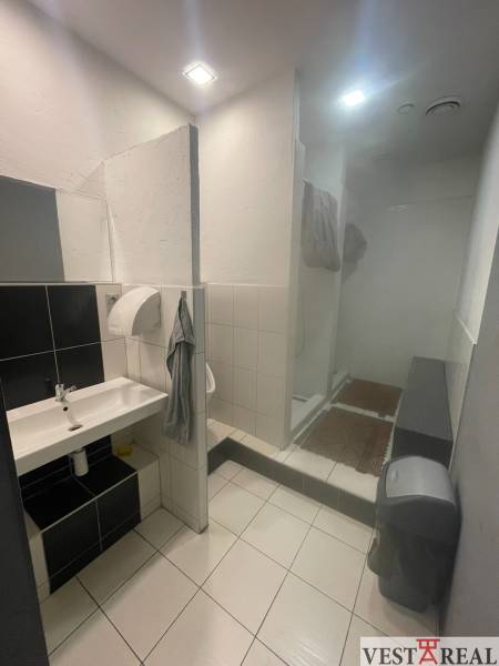 Bathroom in commercial premises with a sink, shower, and light-colored tiles.