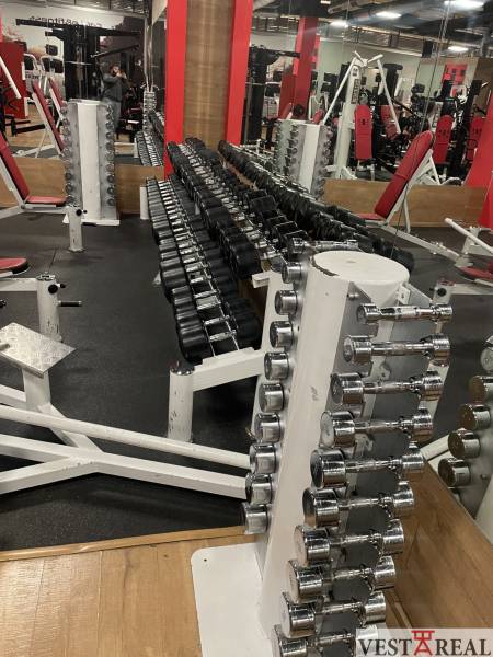 Dumbbells and fitness equipment on a glossy wooden-decor floor in commercial premises.